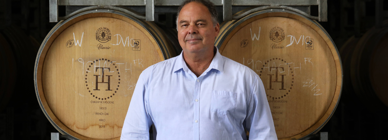 A man posing in front of Tumblong Hills wine barrels 